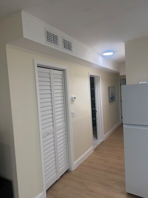 A hallway with a white refrigerator, a door with a window, and a wall-mounted thermostat. - Coastal Haven Getaway 2 (Treasure Island)