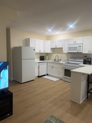 A modern kitchen with white cabinets, a refrigerator, a microwave, a stove, and a coffee maker. - Coastal Haven Getaway 2 (Treasure Island)