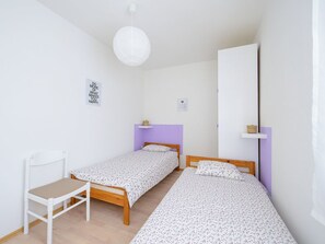 Ein kleines, sauberes Zimmer mit zwei Einzelbetten, einem weißen Stuhl und einer weißen Deckenleuchte.