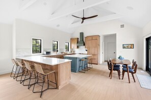 Una cocina moderna con una isla grande, taburetes de bar, armarios de madera y un ventilador de techo.