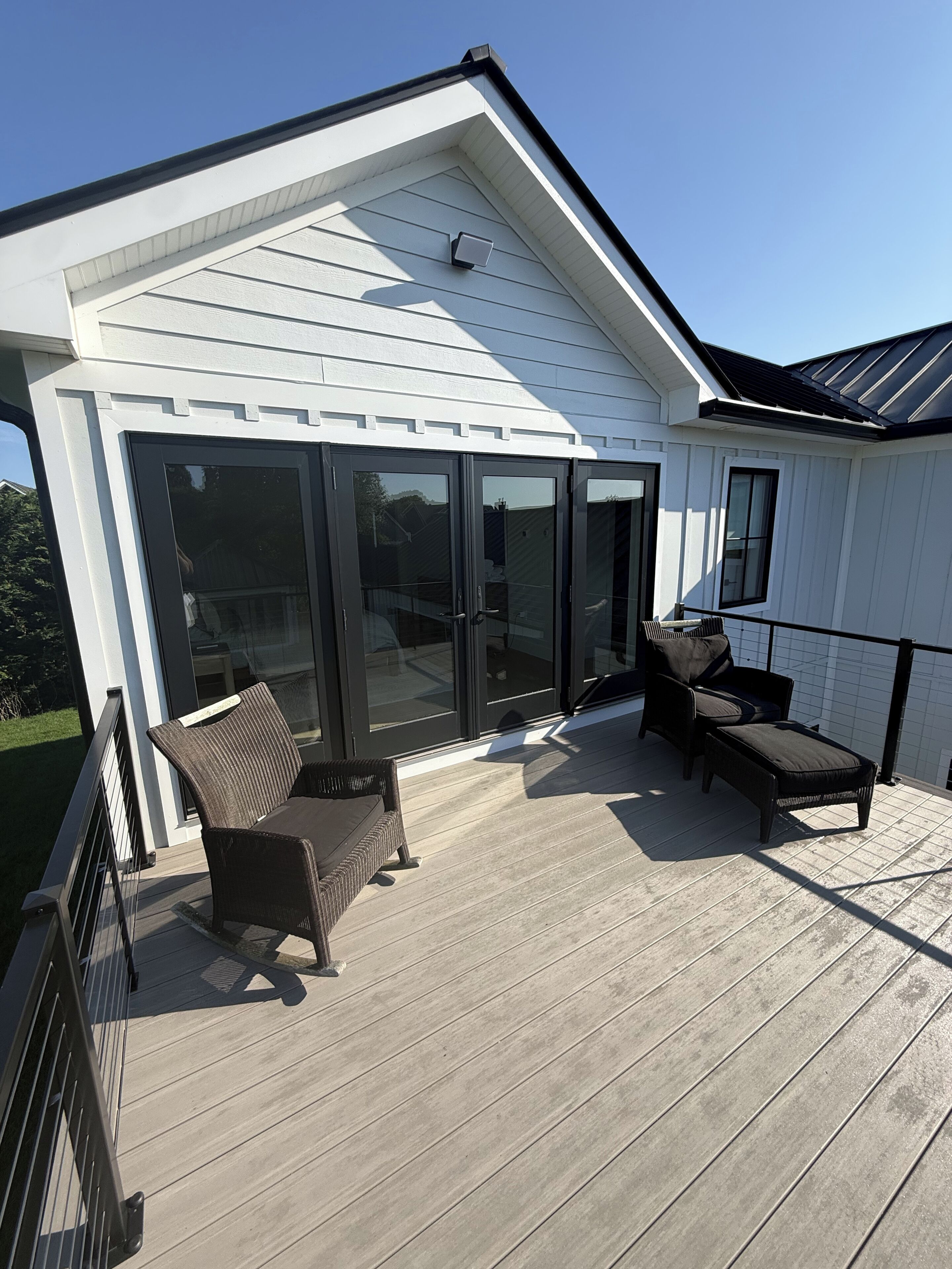 Une terrasse couverte avec deux fauteuils en osier et un banc, une porte-fenêtre coulissante et un mur extérieur blanc.