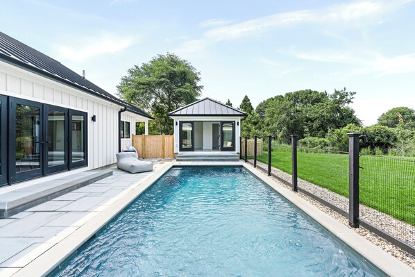 A swimming pool with a modern house and a fenced garden area.