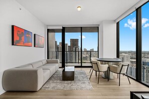 A modern living room with a sofa, coffee table, and dining area with chairs. Large windows offer a city view. - Brand New E11even Residences Suite with Ocean View (Miami)