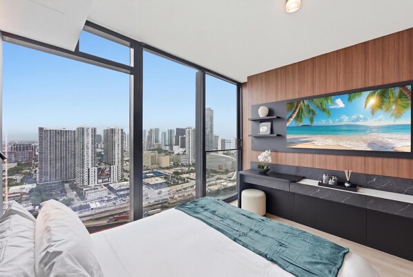 Ein Schlafzimmer mit großem Fenster, einem Bett, einem Fernseher und Blick auf die Stadt.