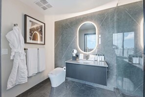Ein modernes Badezimmer mit Marmorwand, einem großen Spiegel, einem Waschtisch mit Toilettenartikeln und einem weißen Bademantel, der an der Wand hängt.