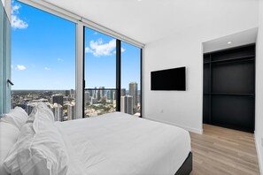 A bedroom with a large bed, a TV mounted on the wall, and a city view through large windows. - 46th Floor Exclusive 2BR Luxury Residence at The E11even (Miami)