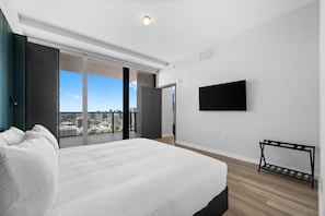 A modern bedroom with a large bed, a TV mounted on the wall, and a balcony with a city view. - Exclusive 2BR Luxury Residence at The E11even (Miami)
