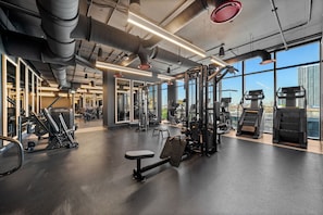 Ein Fitnessstudio mit Trainingsgeräten, großen Fenstern und Blick auf eine Stadtlandschaft.