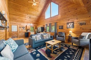Interior acogedor de una cabaña con techo de madera, un sofá, sillones, una mesa de centro y una alfombra.