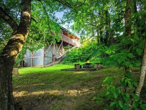 A modern building with a glass facade, surrounded by lush greenery and a grassy area with a fire pit. - Creekside Villa Retreat with Hot Tub, Fire Pit and Playground (Sevierville)