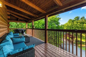 A covered deck with a wooden railing, a sofa with cushions, and a grill. - Creekside Villa Retreat with Hot Tub, Fire Pit and Playground (Sevierville)