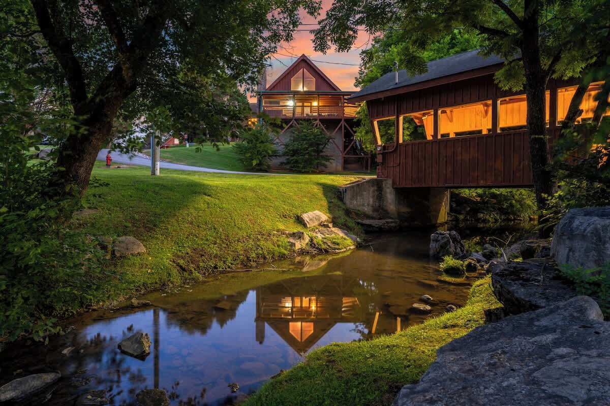 A wooden cabin with a balcony overlooking a pond, surrounded by greenery.