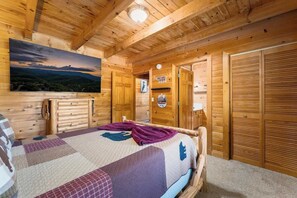 A wooden cabin room with a bed, a painting of a landscape, and a sign on the wall. - Creekside Villa Retreat with Hot Tub, Fire Pit and Playground (Sevierville)