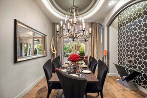 Un espace repas agrémenté d’un lustre, d’un miroir et d’un mur orné de motifs.