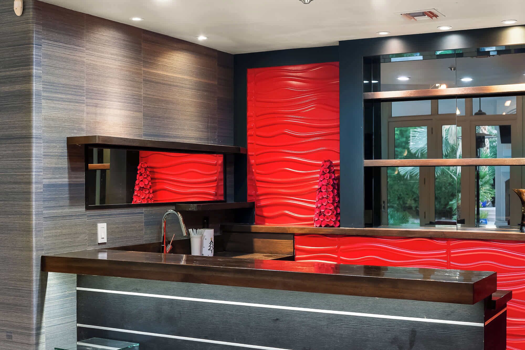 A modern bathroom with a large mirror, a wooden vanity, and a red textured wall.