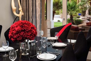 A dining table set for two with a bouquet of red roses, clear glassware, and a view of a landscaped outdoor area. - $5Mil Luxury Estate - Pickleball Pool Hot Tub (Scottsdale)