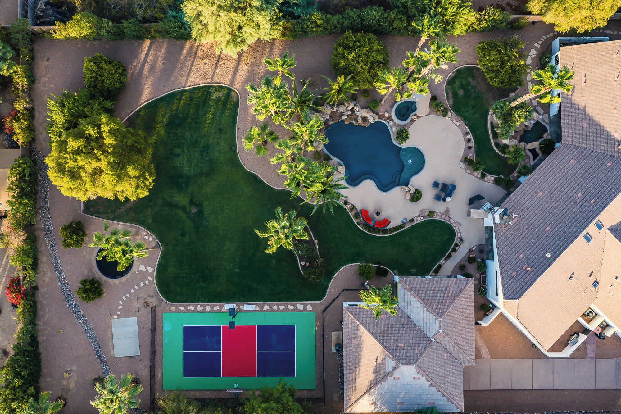 An aerial view of a property with a tennis court, multiple pools, and landscaped areas.