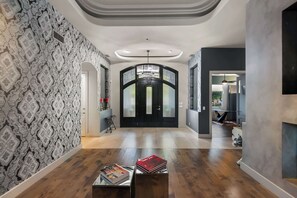 A hallway with patterned wallpaper, a black door with glass panels, and a magazine on a table. - $5Mil Luxury Estate - Pickleball Pool Hot Tub (Scottsdale)