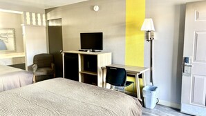 Una habitación de hotel con cama, escritorio, televisor, una silla y una lámpara.
