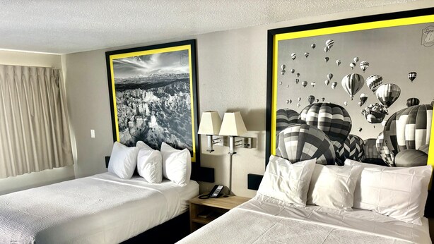 Una habitación de hotel con dos camas, una mesita de noche con una lámpara y una pared con una fotografía grande en blanco y negro.