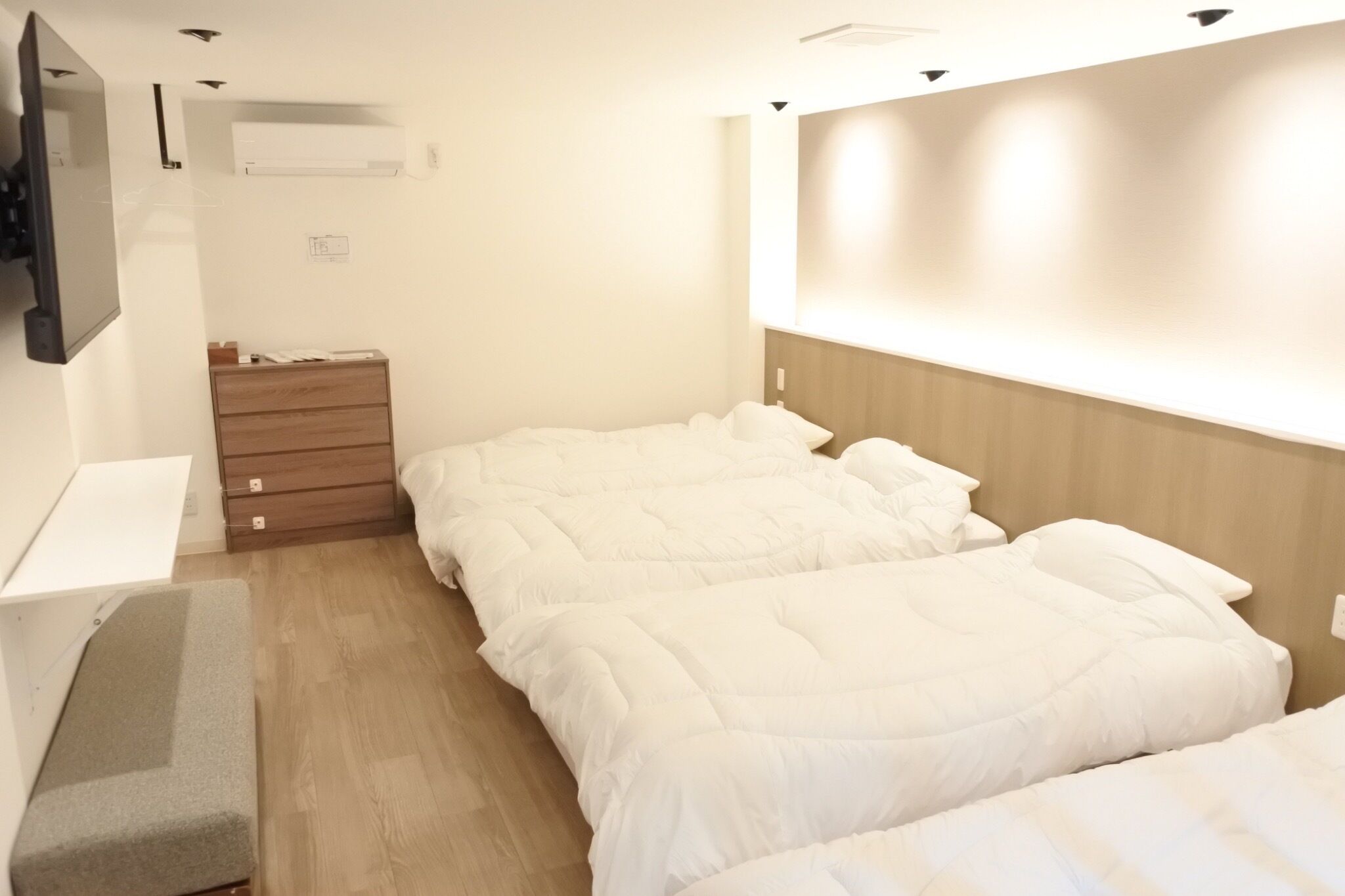 A hotel room with two beds, a wooden dresser, a desk, and a wall-mounted TV.