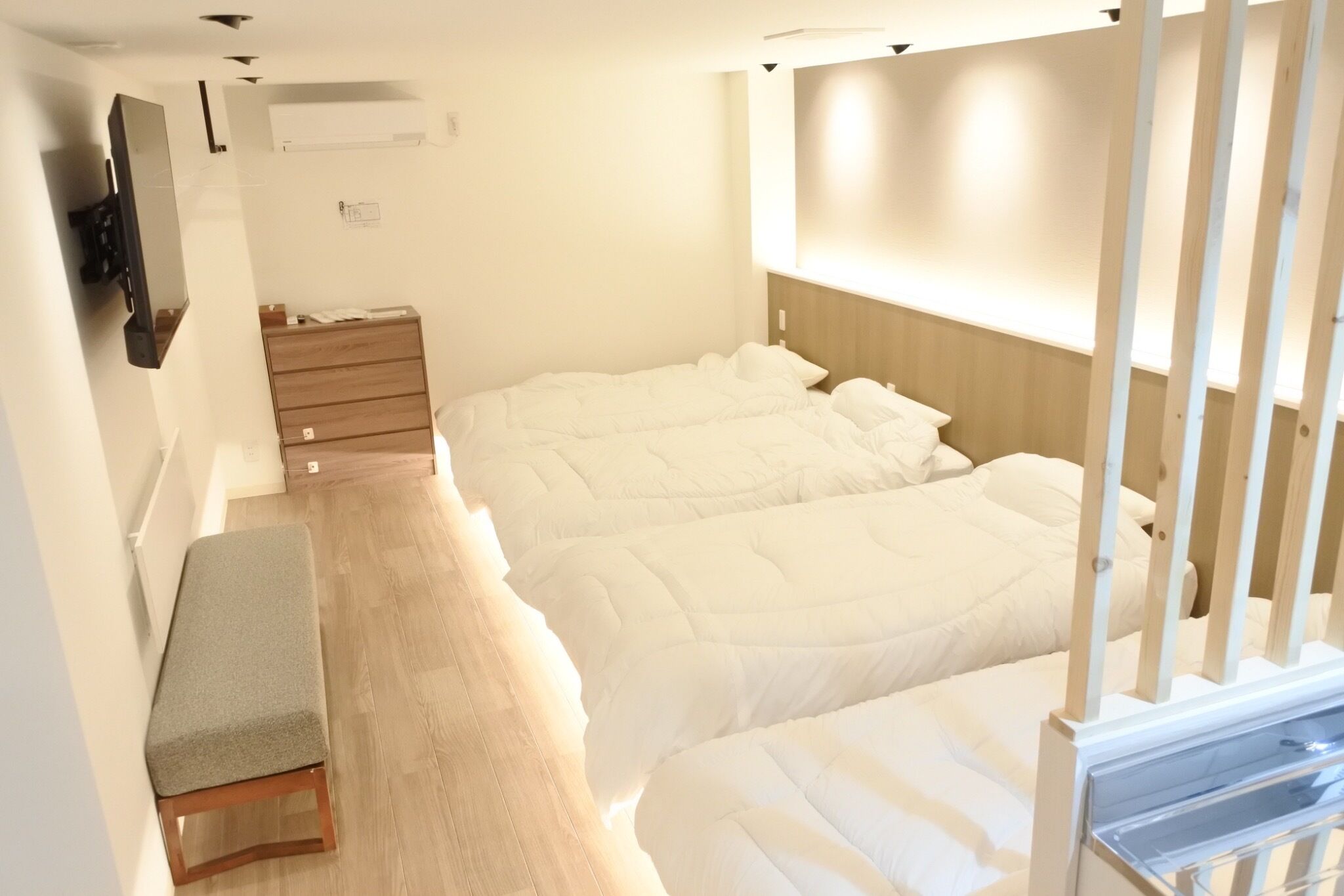 A hotel room with a bed, a bedside table, a wall-mounted TV, and a wooden dresser.