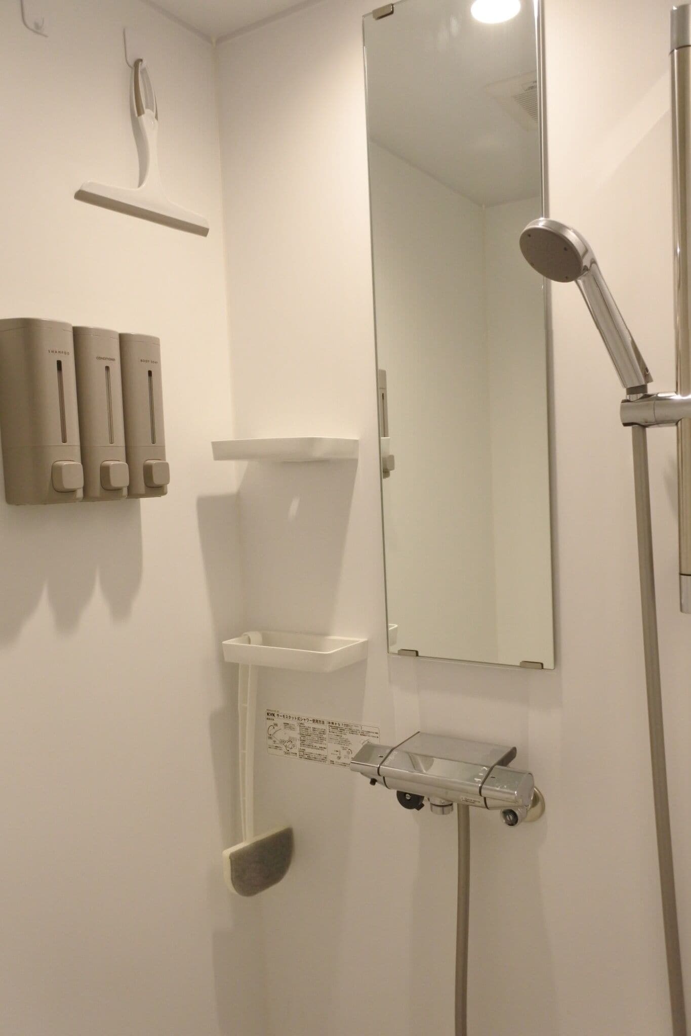 A bathroom with a toilet, a mirror, a handheld showerhead, and a soap dispenser.