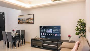 Una sala de estar moderna con un televisor de pantalla plana, una mesa de comedor con sillas, un sofá y un cuadro en la pared.