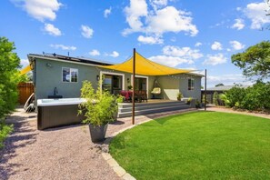 Ein modernes Haus mit Whirlpool, überdachter Terrasse und gepflegtem Rasen.