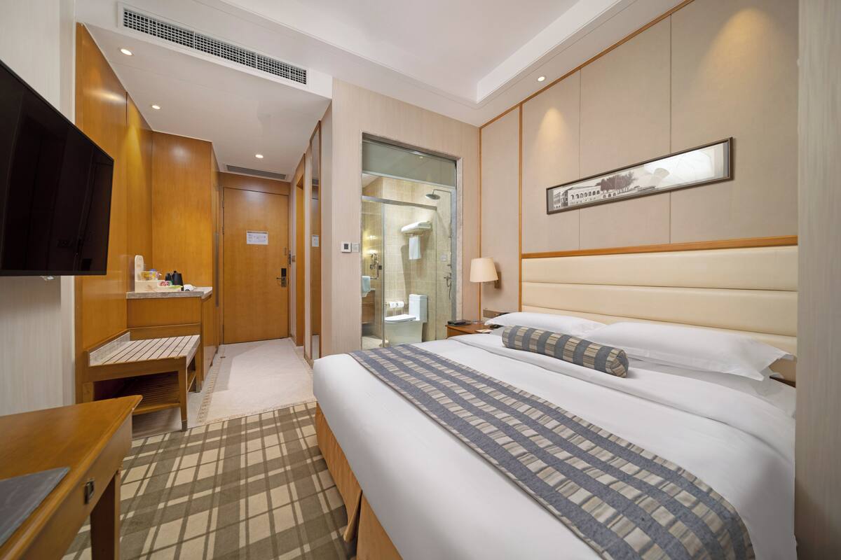 A hotel room with a bed, bedside table, TV, and a bathroom visible through an open door.