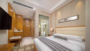 A hotel room with a bed, bedside table, TV, and a bathroom visible through an open door.