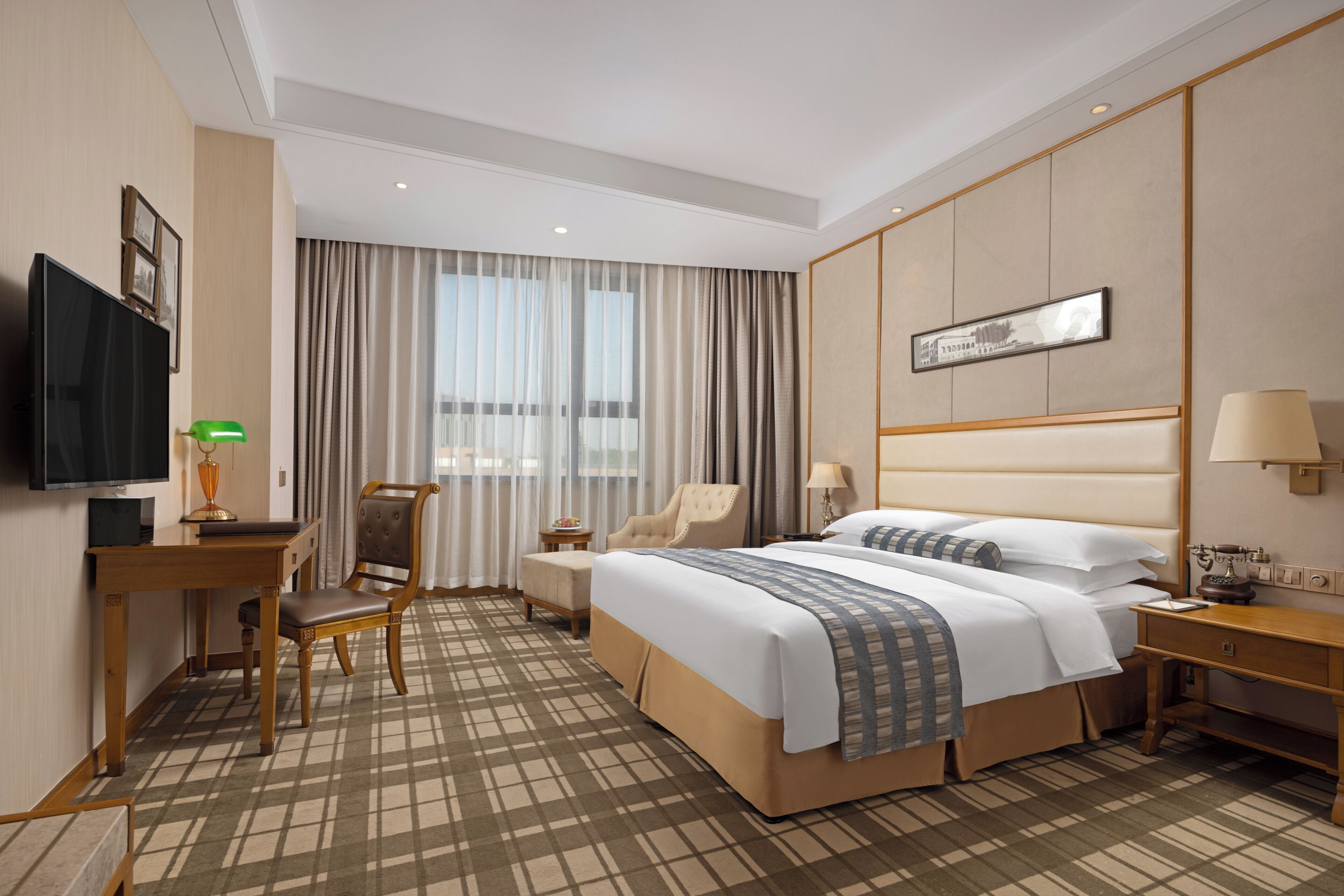 A hotel room with a large bed, a desk with a chair, a television, and a window with curtains.
