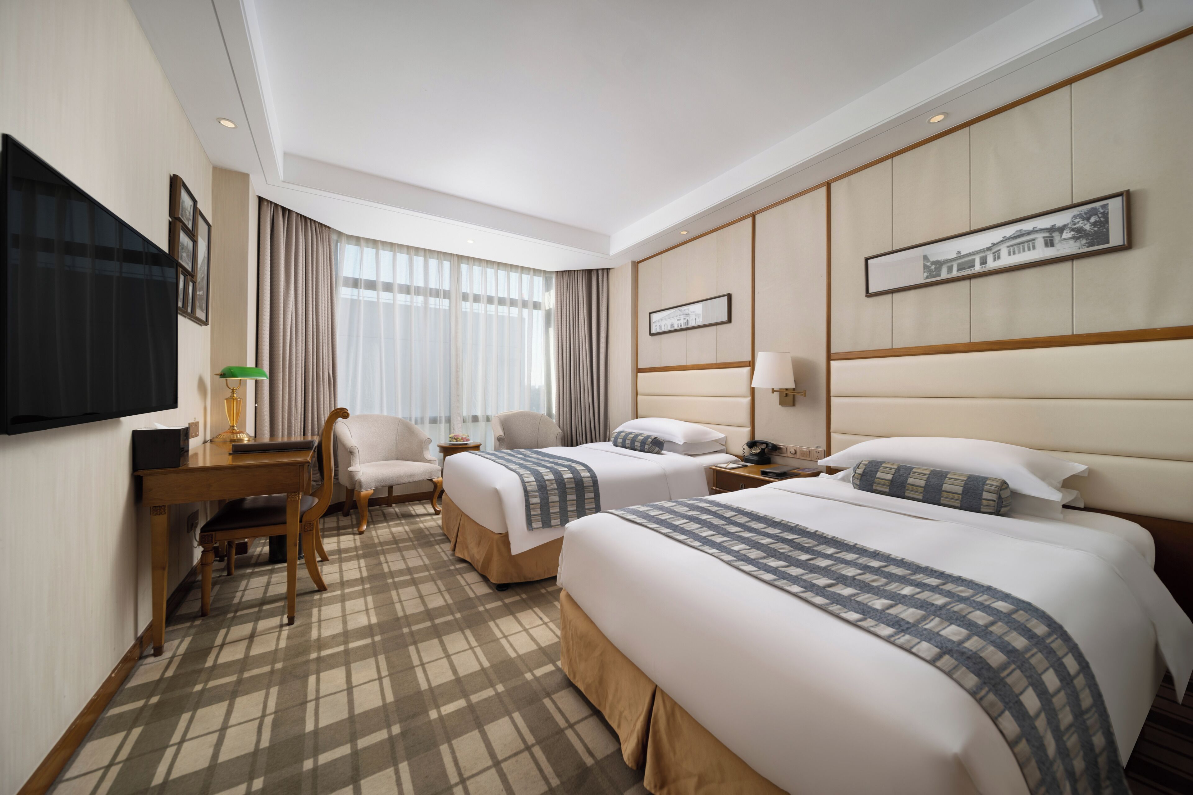 A hotel room with two beds, a desk with a chair, a television, and a window with curtains.