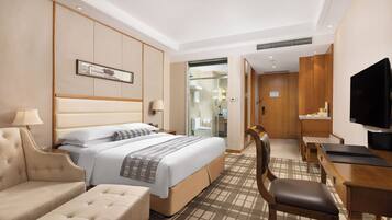 A hotel room with a bed, a desk, a chair, a television, and a bathroom with a shower and toilet.