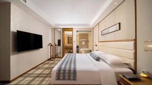 Hotellihuone, jossa on suuri sänky, seinälle asennettu taulutelevisio, yöpöytä lampun kanssa ja näkymä kylpyhuoneeseen.