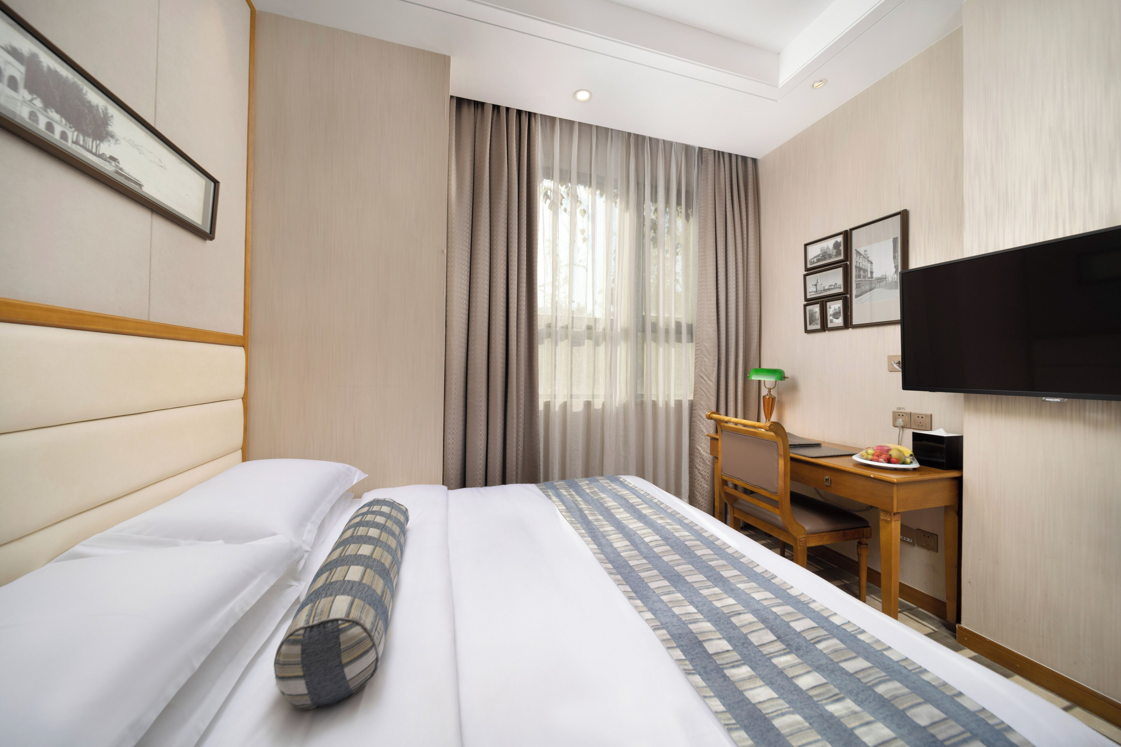 Habitación de hotel con cama, escritorio, silla, televisor y ventana con cortinas.
