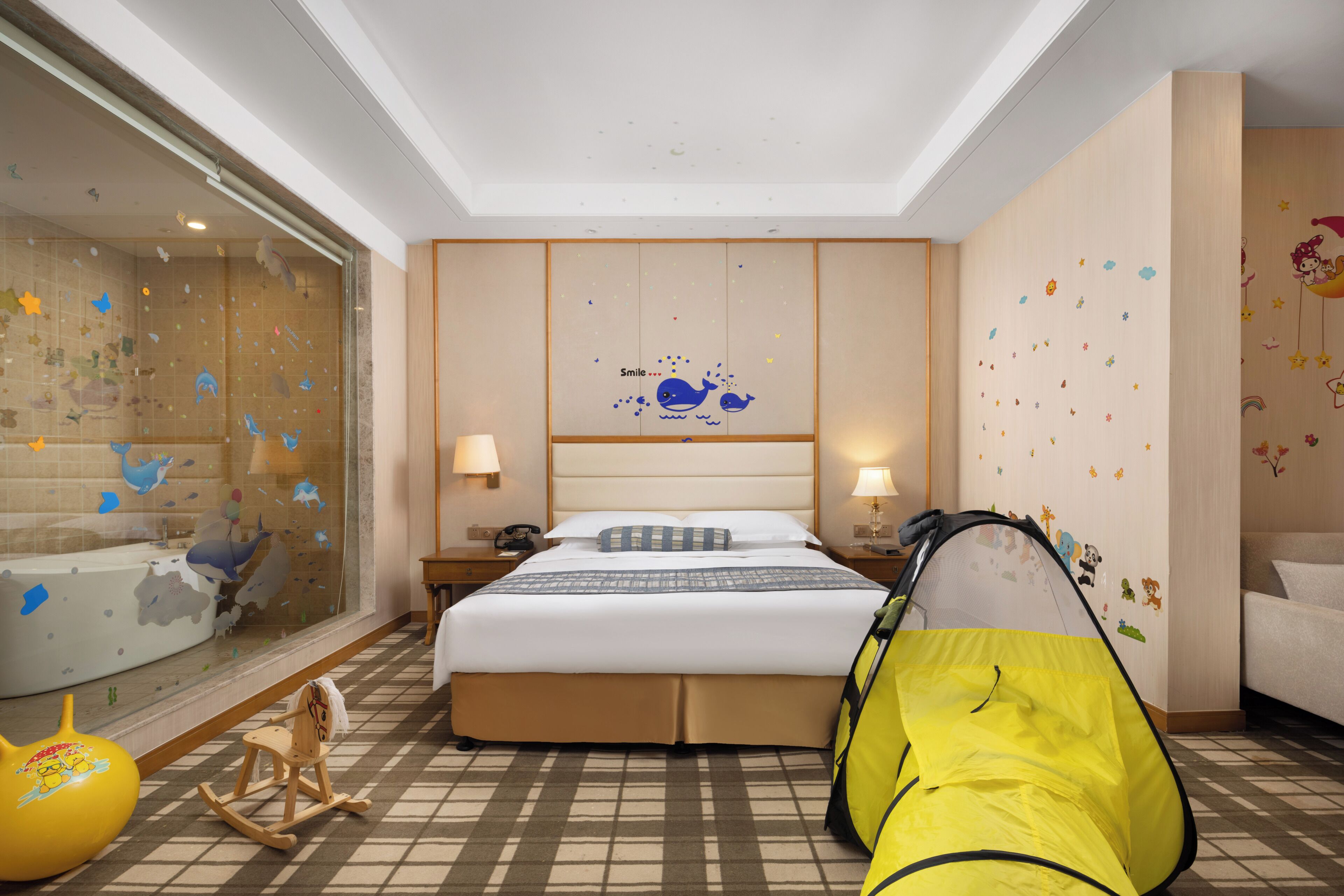 A hotel room with a bed, a tent, a rocking horse, and a wall with star stickers.