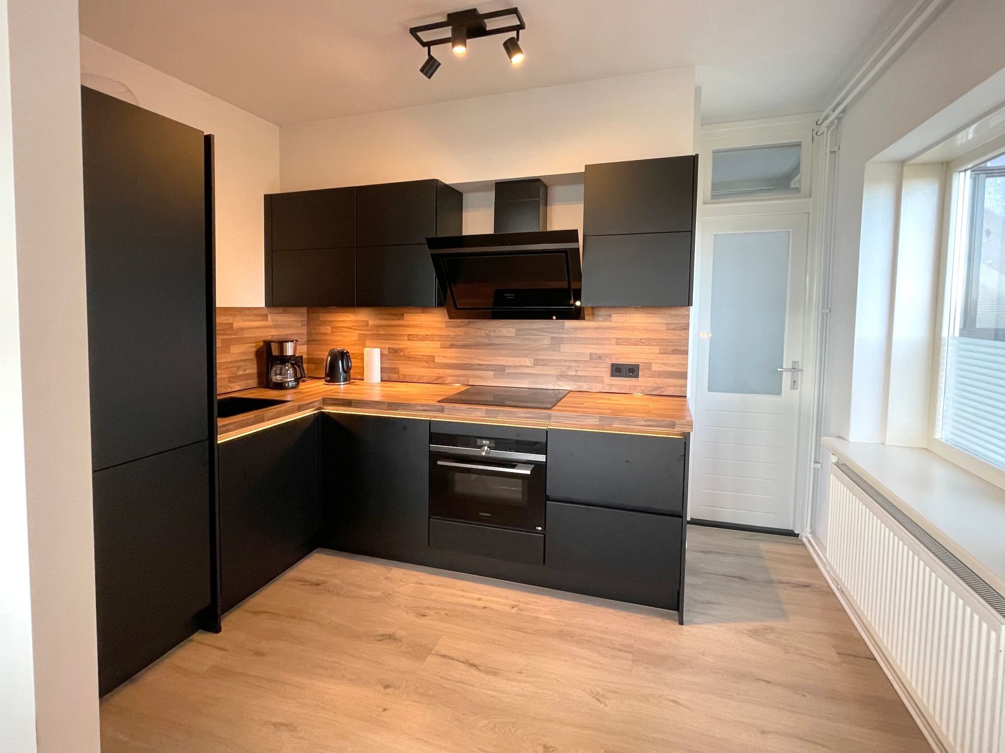 Une cuisine moderne avec des meubles de couleur noire, un plan de travail en bois et des appareils électroménagers intégrés.