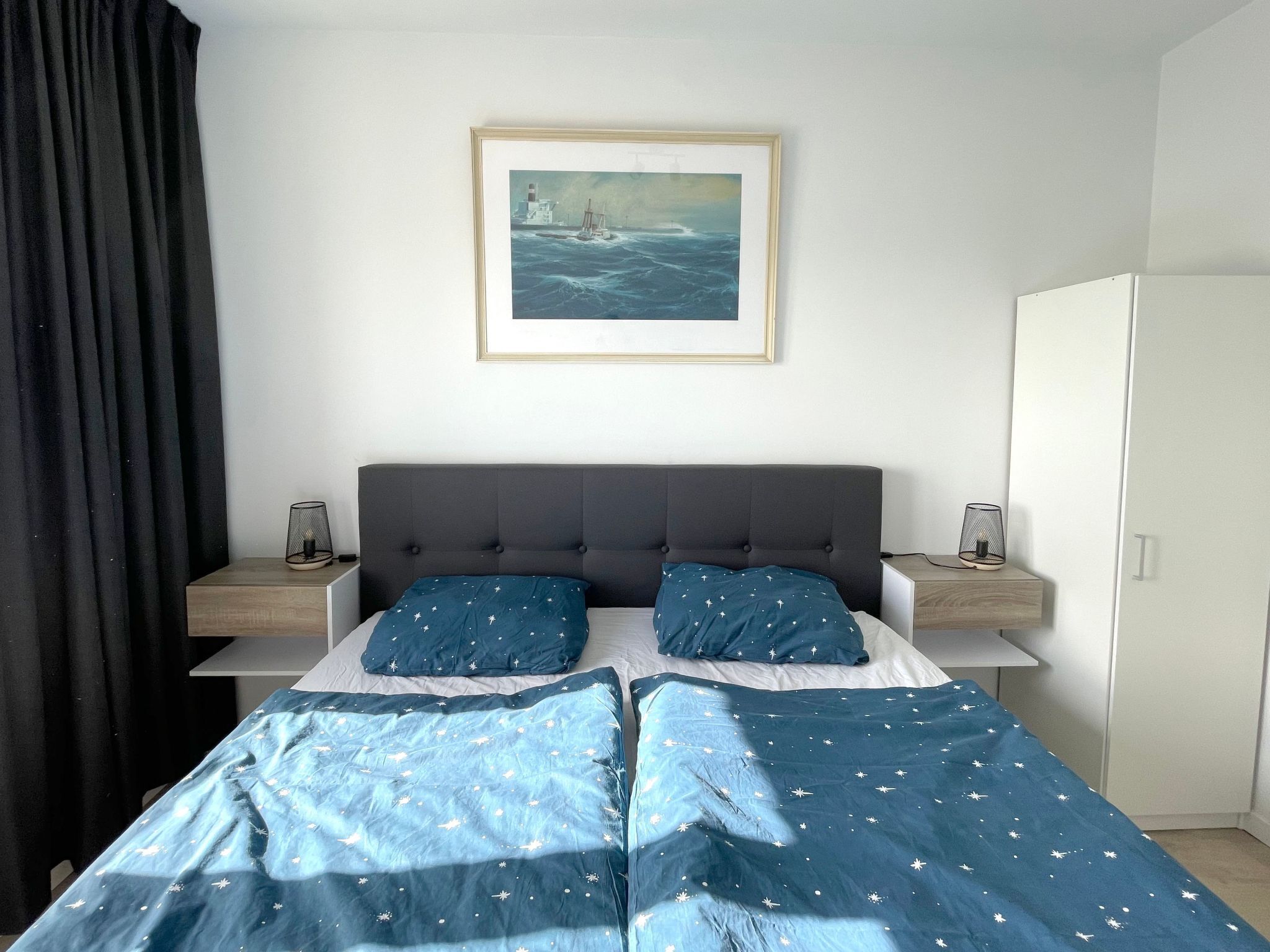 Une chambre à coucher comprenant un lit, deux tables de chevet, une commode, un tableau encadré au mur et une armoire.