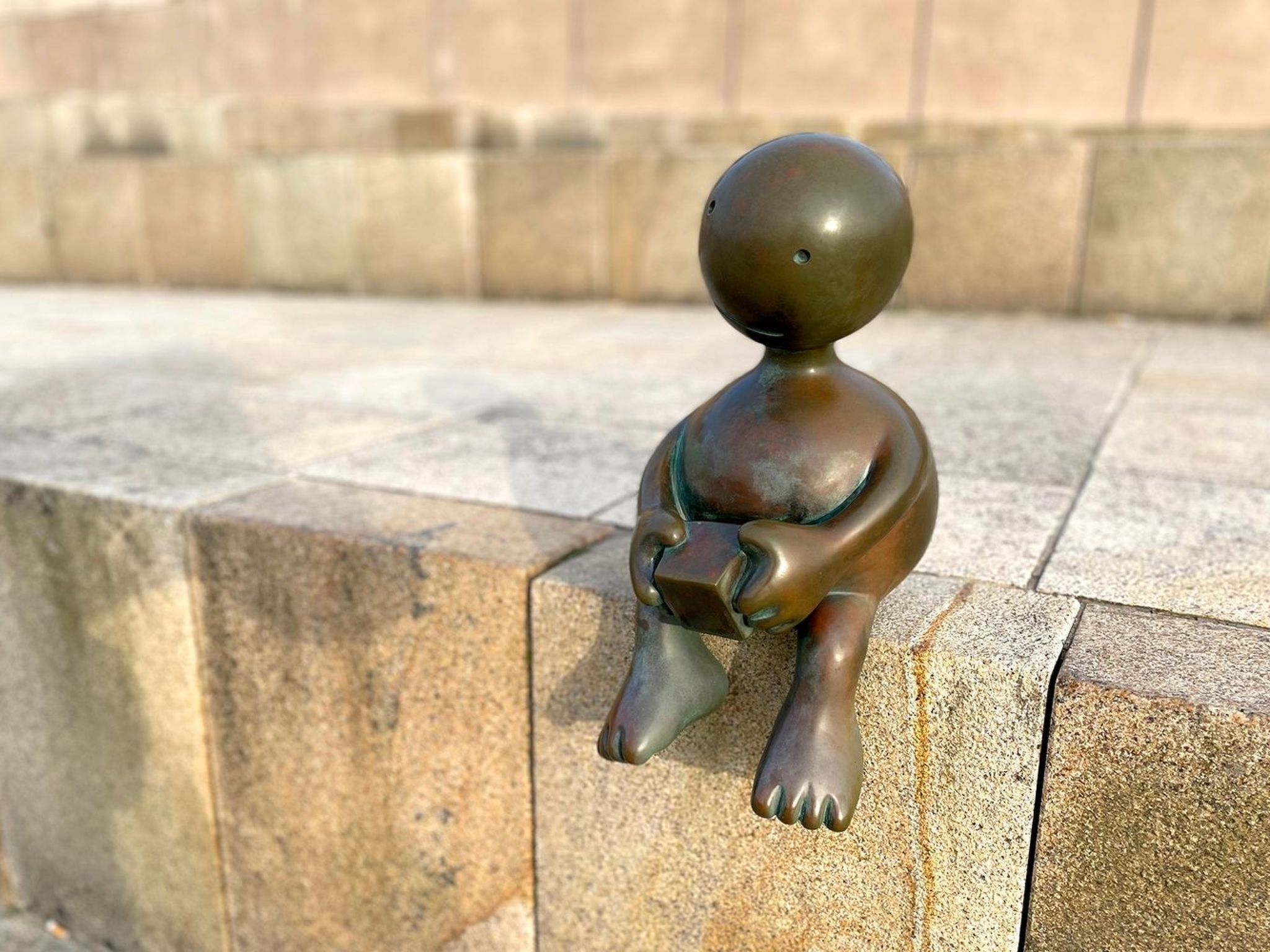 A bronze statue of a seated figure holding a book, placed on a stone ledge.