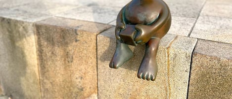 A bronze statue of a seated figure holding a book, placed on a stone ledge.