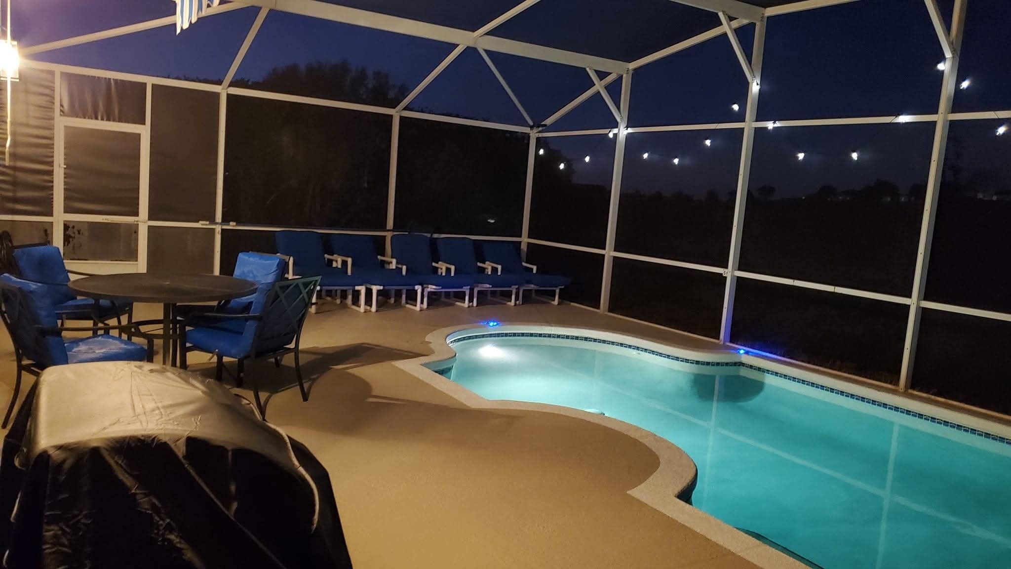 An indoor swimming pool with a covered area, blue chairs, and a table.
