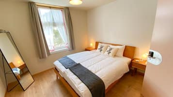 Ein Schlafzimmer mit einem Bett, Nachttischlampen, einem Fenster mit Vorhängen, einem Spiegel und einem Holzboden.
