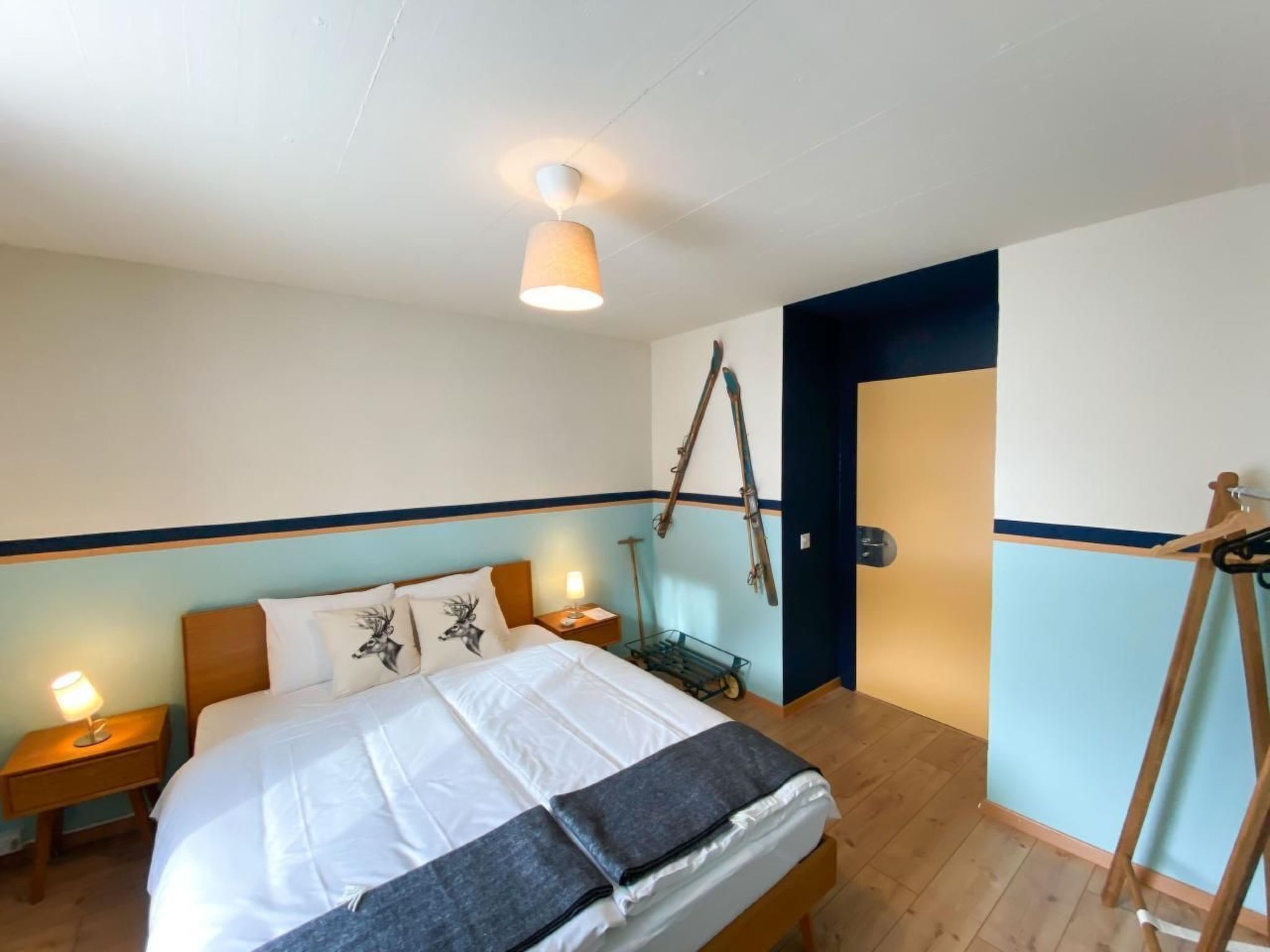 A bedroom with a bed, bedside lamps, a wooden floor, a wall-mounted rack, and a door.