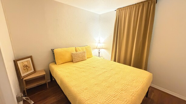 Um quarto com uma cama, mesa de cabeceira, abajur e cortina.