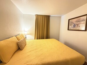 Ein Hotelzimmer mit Bett, Lampe, Gemälde und einem Fenster mit Vorhängen.