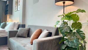 Uma sala de estar moderna com um sofá cinzento, um abajur preto e uma grande planta verde.
