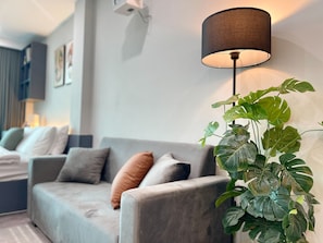A modern living room with a grey sofa, a black floor lamp, and a large green plant.