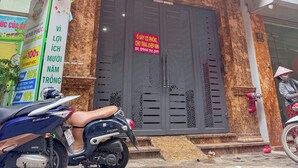 Um edifício com uma porta de entrada grande e escura, uma varanda com guarda-corpo de metal e uma scooter estacionada em frente.