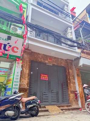 A building with a large, dark entrance door, a balcony with a metal railing, and a scooter parked in front.